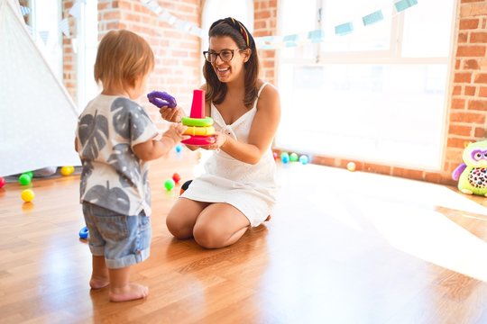 Beautiful teacher and toddler building pyramid using hoops around lots of toys at kindergarten