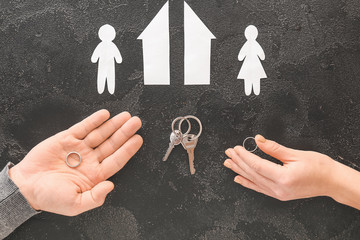 Male and female hands with wedding rings, keys, cut figures of house and couple on dark background. Concept of divorce - obrazy, fototapety, plakaty
