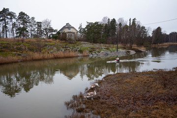 Obraz premium An old authentic rural house and flying trees on the island of Seurasaari is reflected in the lake water on a gloomy autumn day in Helsinki in Finland. Finland autumn landscape