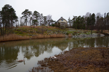 Obraz premium An old authentic rural house and flying trees on the island of Seurasaari is reflected in the lake water on a gloomy autumn day in Helsinki in Finland. Finland autumn landscape