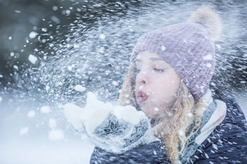 Beautiful young woman in warm clothing blowing snow