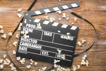 Tasty popcorn with movie clapper on wooden background
