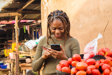 young african woman selling in a local african market using her mobile phone and credit card