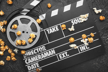Tasty popcorn with movie clapper and film on dark background