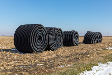 Coiled rolls of black perforated plastic drainage pipe, field tile, sitting in farm field after...