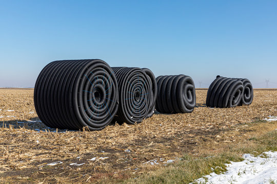 Coiled Rolls Of Black Perforated Plastic Drainage Pipe, Field Tile, Sitting In Farm Field After Harvest Ready To Be Buried Underground During Winter