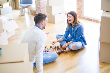 Fototapeta na wymiar Young beautiful couple playing chess at new home around cardboard boxes