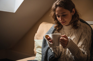 Beautiful young woman drinking coffee in a room with winter clothes