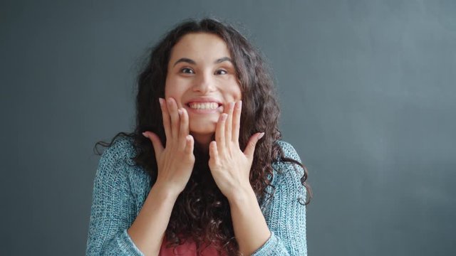 Slow motion of happy girl laughing clapping hands feeling surprised indoors on black background. Joyful people, emotions and excitement concept.