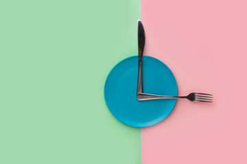 Empty blue plate with fork and knife imitating arrows on clock on duotone chartreuse pink background. Healthy diet meal planning weight loss concept. Creative foot poster with copy space