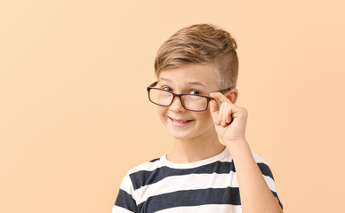 Cute little boy with eyeglasses on color background