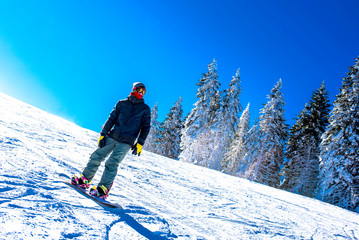 Active snowboarder riding down the hill in mountain ski resort. Winter sports concept