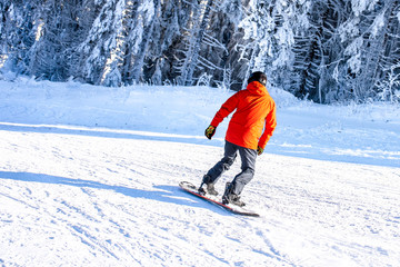 Fototapeta na wymiar Back view of snowboarder riding down the ski slope in mountain ski resort