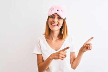 Beautiful redhead woman wearing sleeping mask over isolated background smiling and looking at the...