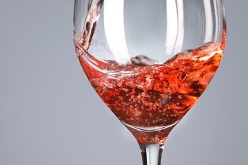 Pouring of tasty wine in glass against grey background, closeup