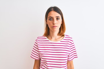 Beautiful redhead woman wearing casual striped pink t-shirt over isolated background with serious expression on face. Simple and natural looking at the camera.