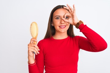 Young beautiful girl holding hair comb standing over isolated white background with happy face...
