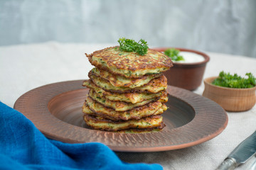 Zucchini fritters. Vegetarian zucchini pancakes with fresh herbs and sour cream. A stack of pancakes. Dining table. Balance healthy food. Light background.