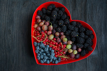 Set of fresh fruits blackberry, gooseberries, red currants, blueberries in a red heart box. Valentine's day concept. Dark wooden background. Space for text.