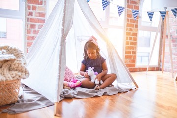 Beautiful toddler girl sitting on the floor playing with unicorn and doll inside  tipi at kindergarten © Krakenimages.com
