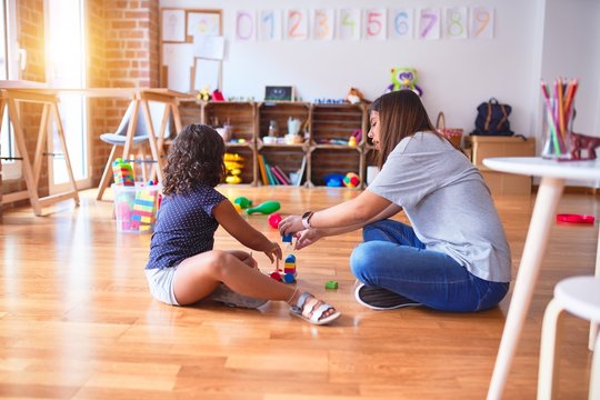 Beautiful teacher and toddler girl playing with train at kindergarten