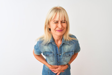 Middle age woman wearing casual denim shirt standing over isolated white background with hand on stomach because indigestion, painful illness feeling unwell. Ache concept.
