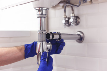 Plumber repairs and maintains chrome siphon under the washbasin. Plumber at work in bathroom,...