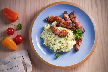 Beef liver wrapped in bacon with mash potato on blue table. Overhead horizontal image