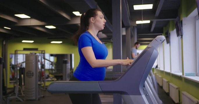 Pregnant young woman doing treadmill exercises in the gym