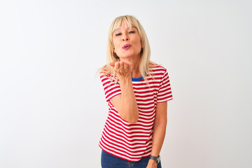 Middle age woman wearing casual striped t-shirt standing over isolated white background looking at the camera blowing a kiss with hand on air being lovely and sexy. Love expression.