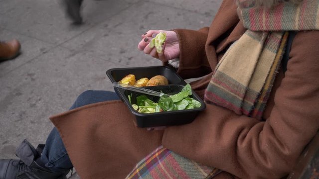 woman eating a satad on city beanch