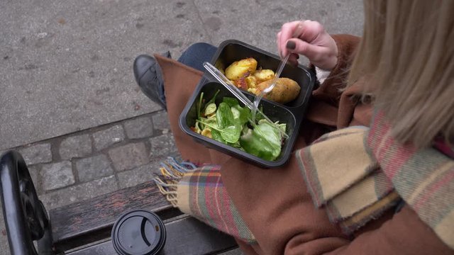woman eating a satad on city beanch