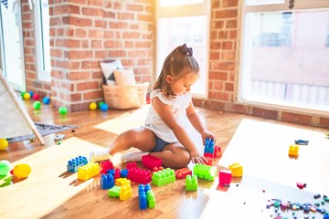 Young beautiful blonde girl kid enjoying play school with toys at kindergarten, smiling happy playing with building blocks at home