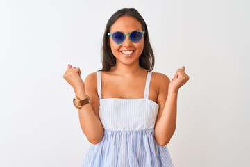Young chinese woman wearing striped dress and sunglasses over isolated white background celebrating surprised and amazed for success with arms raised and open eyes. Winner concept.