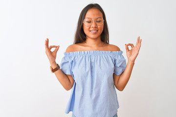 Young chinese woman wearing blue t-shirt and glasses over isolated white background relax and smiling with eyes closed doing meditation gesture with fingers. Yoga concept.