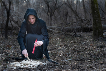 Woman in black robes with Red burning Candle and pile of large wild animal bones in the middle of...