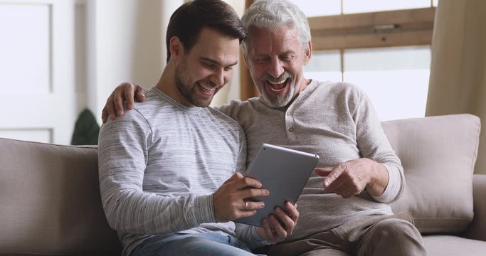 Happy older father and adult son using tablet at home - Powered by Adobe