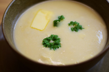Creamy cauliflower soup with cream and butter is decorated with decorative parsley leaves. Modern Norwegian food.