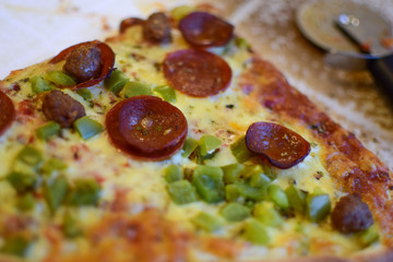 A slice of pizza with salami and a pizza knife are on the kitchen wooden table. Selective focus, bokeh