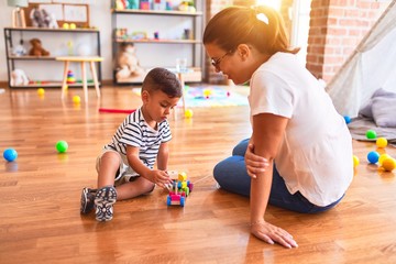 Fototapeta premium Beautiful teacher and toddler boy playing with train at kindergarten