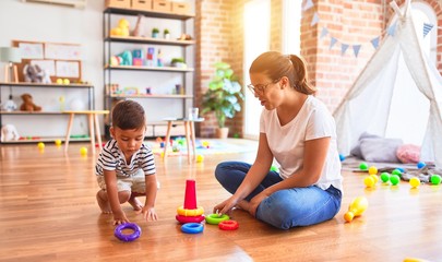 Beautiful teacher and toddler boy building pyramid with hoops bolcks at kindergarten