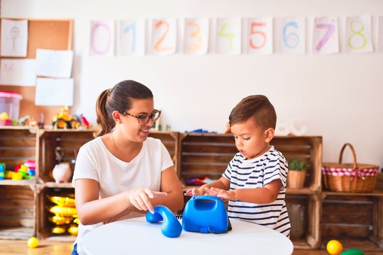 Beautiful teacher and toddler boy playing with vintage blue phone at kindergarten