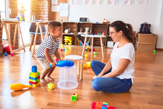 Beautiful teacher and toddler boy playing drum using skitlle and plastic basket at kindergarten