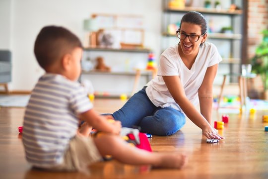 Beautiful teacher and toddler boy playing with tractor and cars at kindergarten