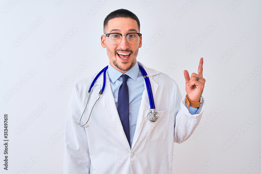 Wall mural Young doctor man wearing stethoscope over isolated background with a big smile on face, pointing with hand finger to the side looking at the camera.