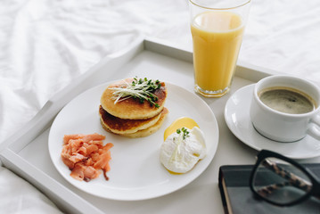 Nutritious and tasty breakfast of pancakes, salmon and poached egg in bed on tray