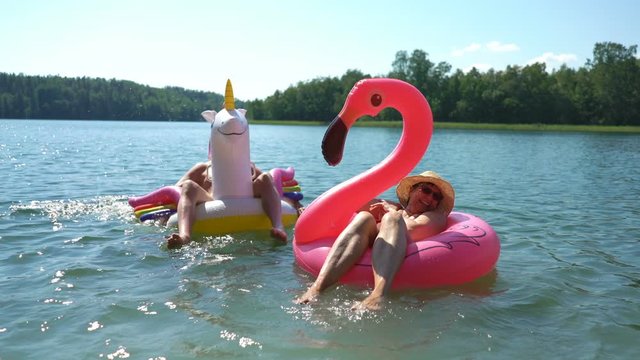 Elderly couple floating on inflatable flamingo and unicorn. Funny active pensioners happy together enjoying summer vacation on the beach in Europe, laughing, playing the fool, splashing water