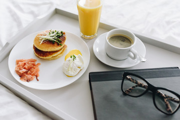 Close up of nutritious and tasty breakfast with coffee in bed on tray with glasses and book