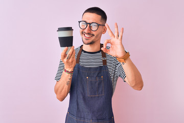 Young handsome barista man wearing uniform over isolated background doing ok sign with fingers, excellent symbol - obrazy, fototapety, plakaty
