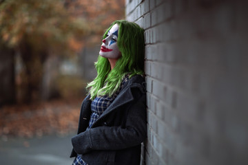 Portrait of a greenhaired girl in chekered dress with joker makeup on a brick wall background. - obrazy, fototapety, plakaty